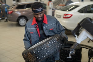 Jovem reparador ou trabalhador de serviço de manutenção transportando roda nova enquanto vai substituí-la em carro ou outro veículo