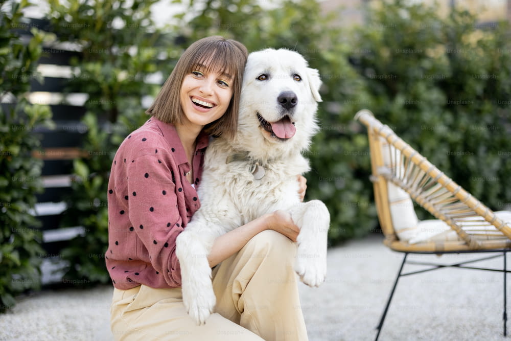 屋外の裏庭で愛らしい白い犬と抱き合う女性のポートレート。ペットとの友情と屋外で幸せな夏の時間を過ごすというコンセプト。マレンマ牧羊犬