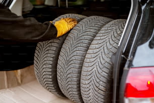 El mecánico trabajador con guantes naranjas está poniendo las ruedas de un automóvil en el maletero de un automóvil con cuidado.