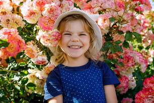 Retrato da menina pequena no jardim de rosas em flor. Bonito lindo adorável criança se divertindo com rosas e flores em um parque no dia ensolarado de verão. Bebê sorridente feliz