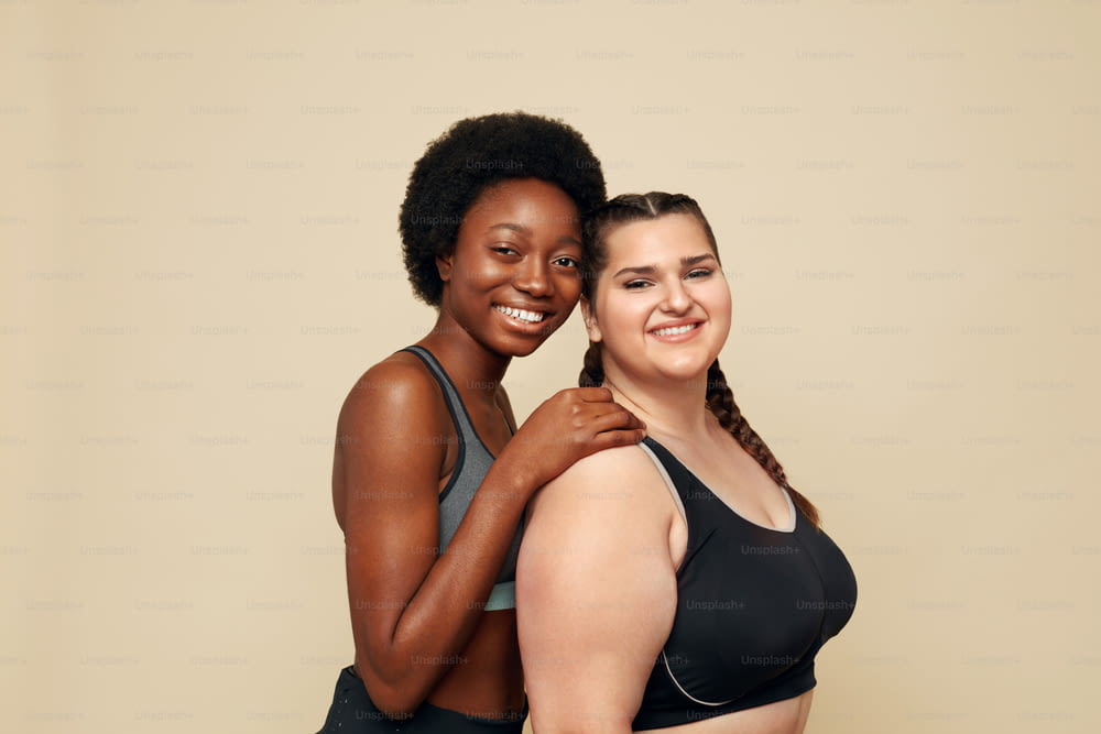 Fitness. Different Ethnicity Women Portrait. Caucasian And African Models In Fitness Clothes Posing On Beige Background. Body Positive As Lifestyle.