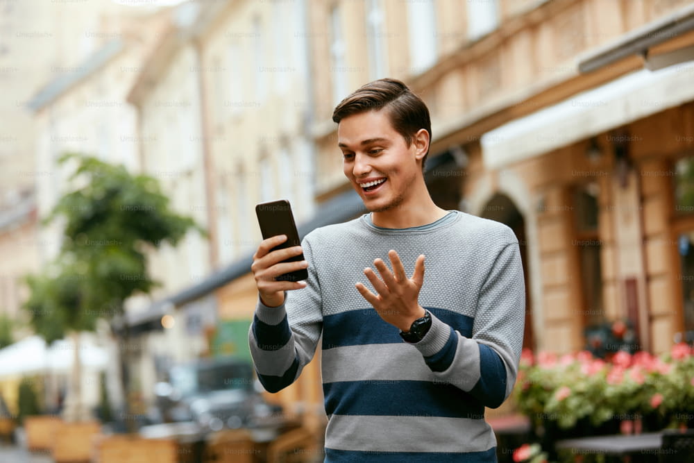 Appel vidéo de l’homme au téléphone dans la rue. Jeune homme souriant utilisant un téléphone portable à l’extérieur. Haute résolution