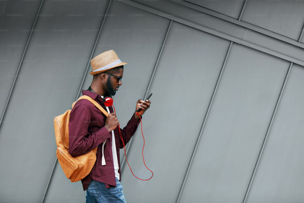 Hübscher schwarzer Mann in modischer Kleidung mit Telefon auf der Straße. Stilvoller afrikanischer Mann mit Kopfhörern und Telefon in der Stadt. Hohe Auflösung