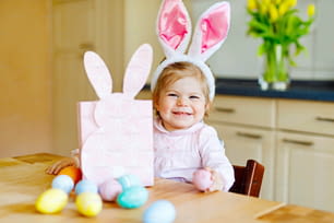 Mignonne petite fille en bas âge portant des oreilles de lapin de Pâques jouant avec des œufs pastel colorés. Happy baby child déballer des cadeaux. Adorable enfant en vêtements roses profitant des vacances.
