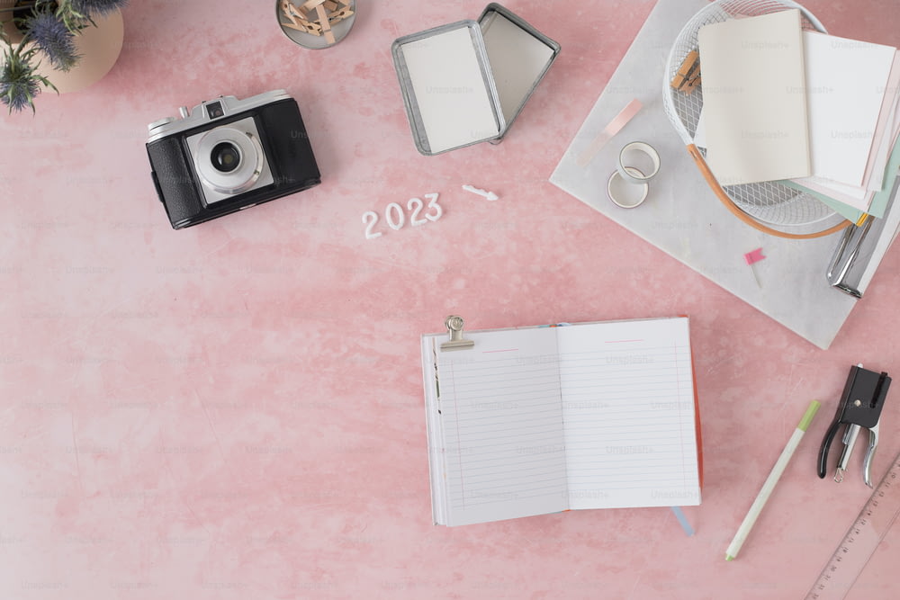 카메라, 공책, 펜이 있는 분홍색 테이블