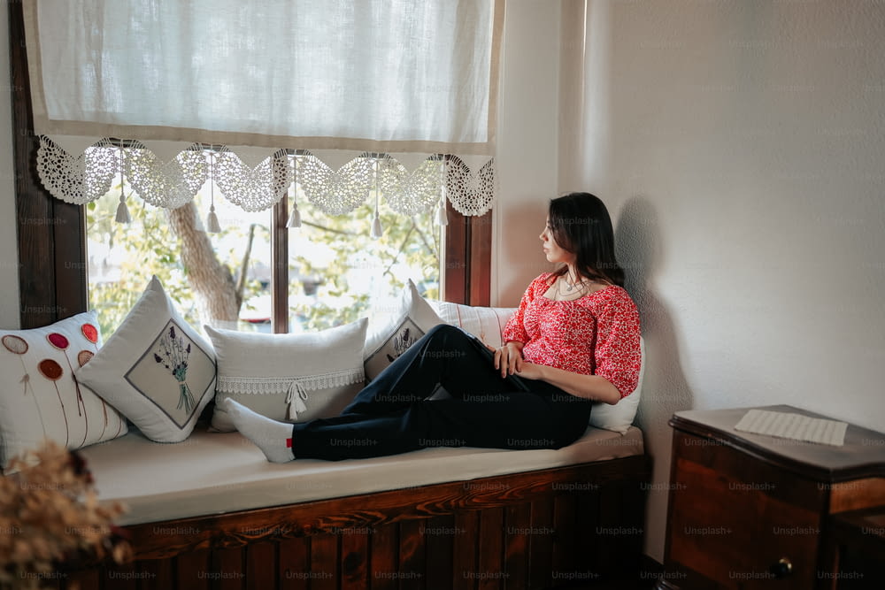 une femme assise sur le rebord d’une fenêtre regardant par la fenêtre