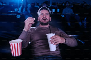 a man sitting in a movie theater holding a drink and popcorn
