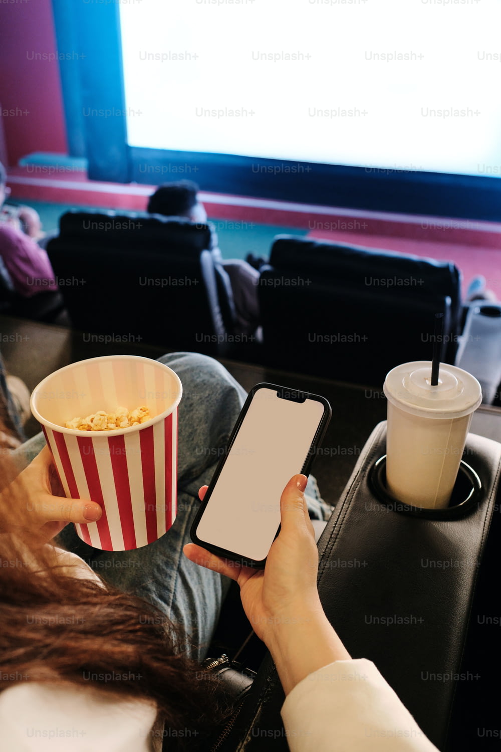 a woman holding a smart phone while sitting in front of a movie screen