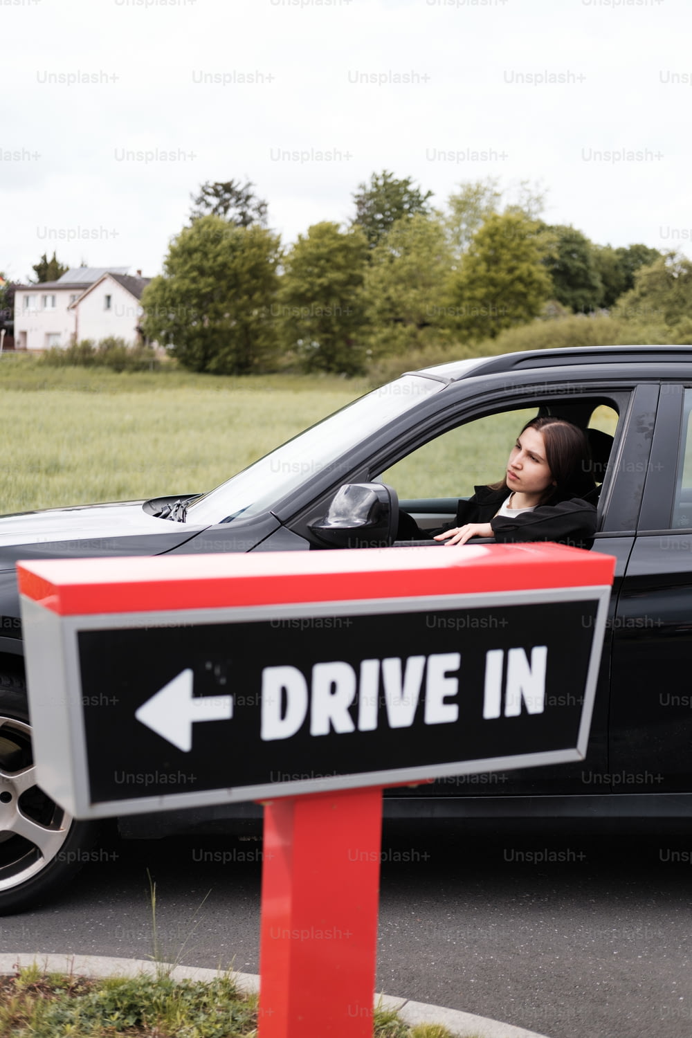 a woman sitting in a car with a drive in sign in front of her