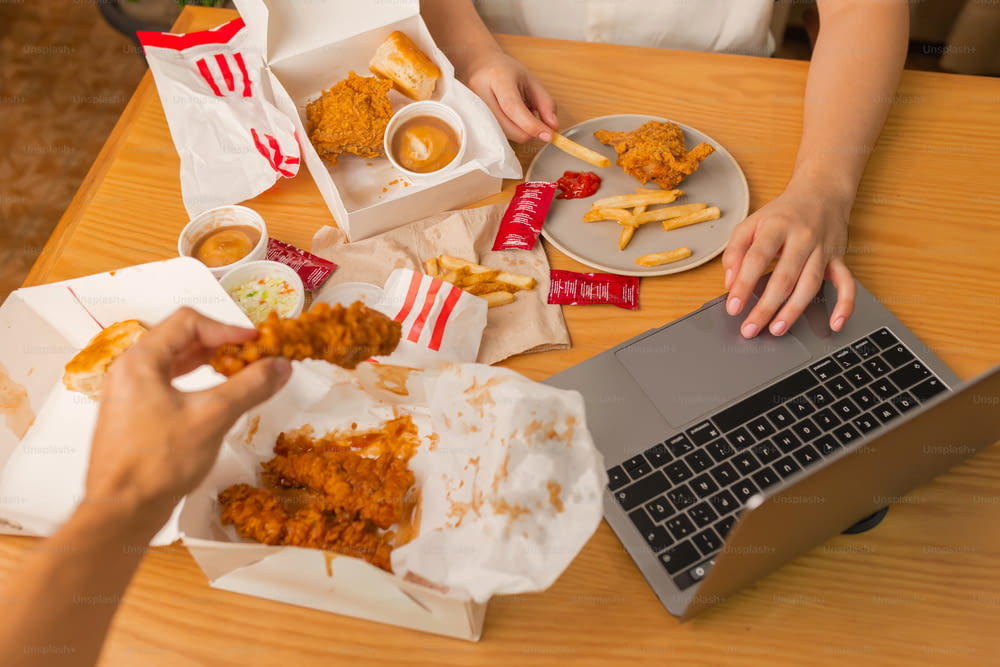 uma pessoa sentada em uma mesa com um pouco de comida e um laptop