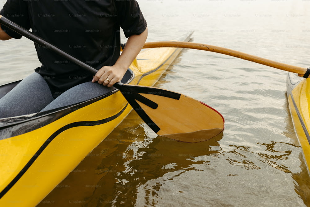 Un hombre con una camisa negra está remando en un kayak amarillo