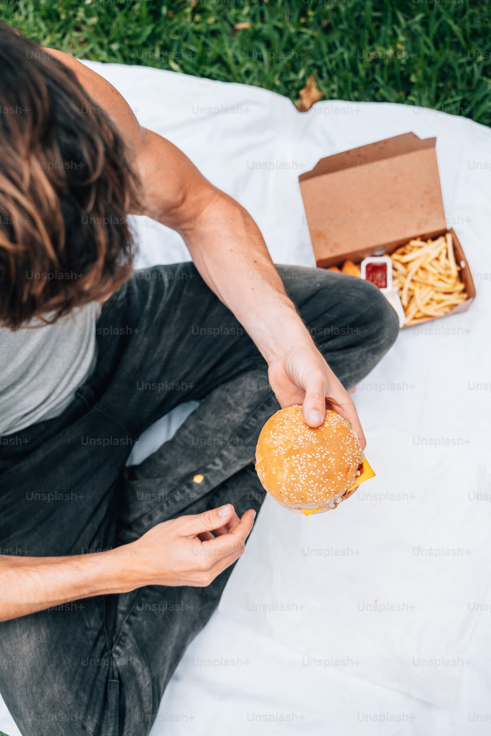 um homem sentado em um cobertor segurando um hambúrguer