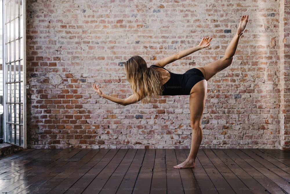 a woman doing a yoga pose in front of a brick wall