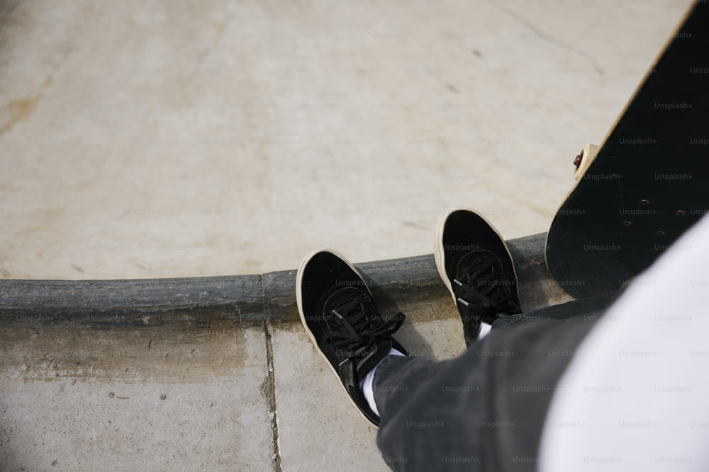 eine Person in schwarzen Schuhen, die neben einem Skateboard steht