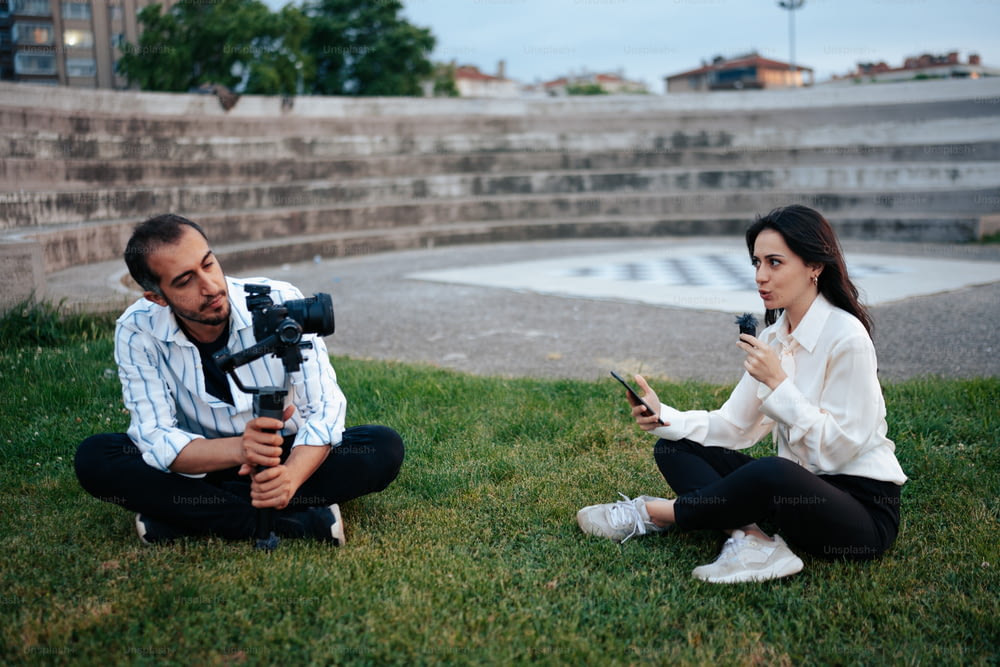 um homem e uma mulher sentados na grama com uma câmera