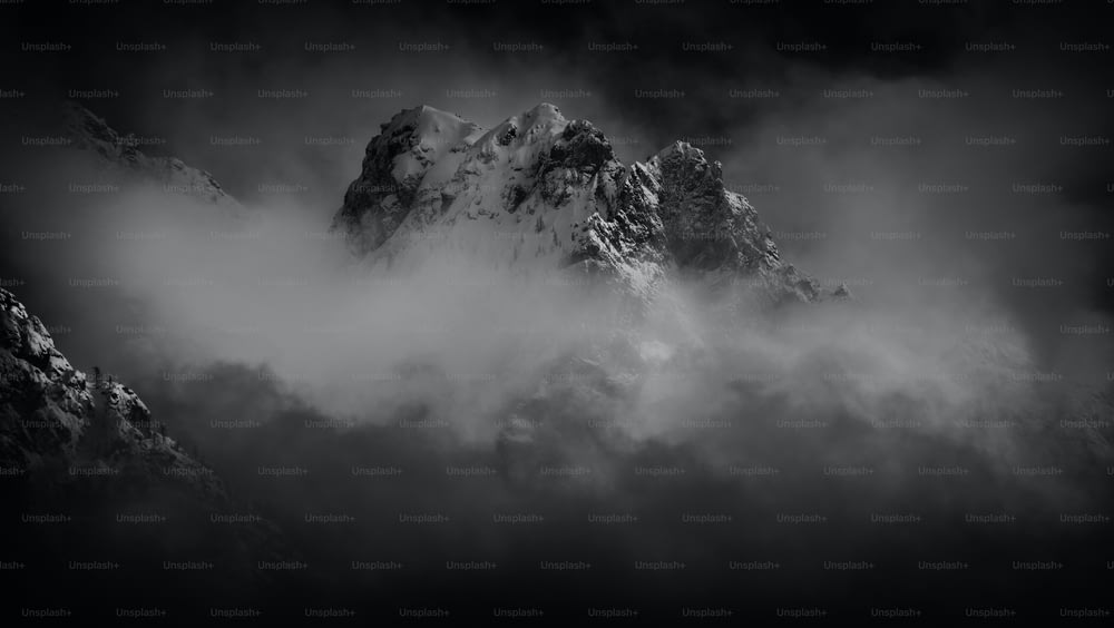 a black and white photo of a mountain covered in clouds