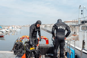 a couple of men in wet suits standing next to a boat