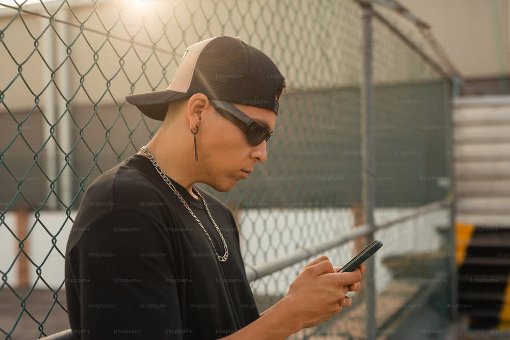 um homem de boné de beisebol e óculos escuros olhando para um celular