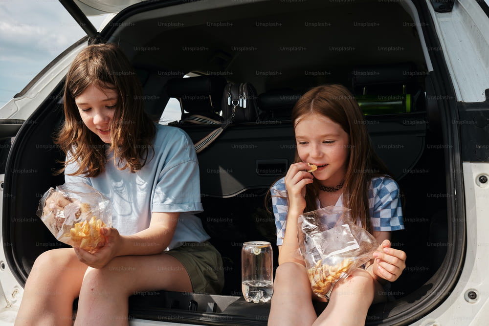 車の後ろに座って食事をする2人の女の子