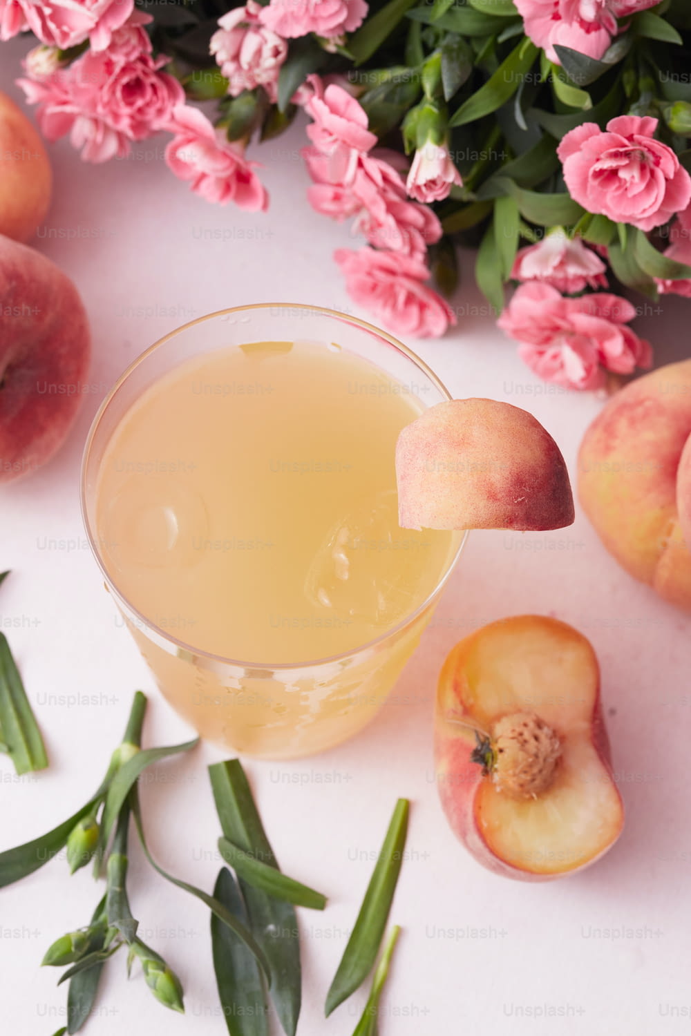 a glass filled with liquid next to peaches and flowers
