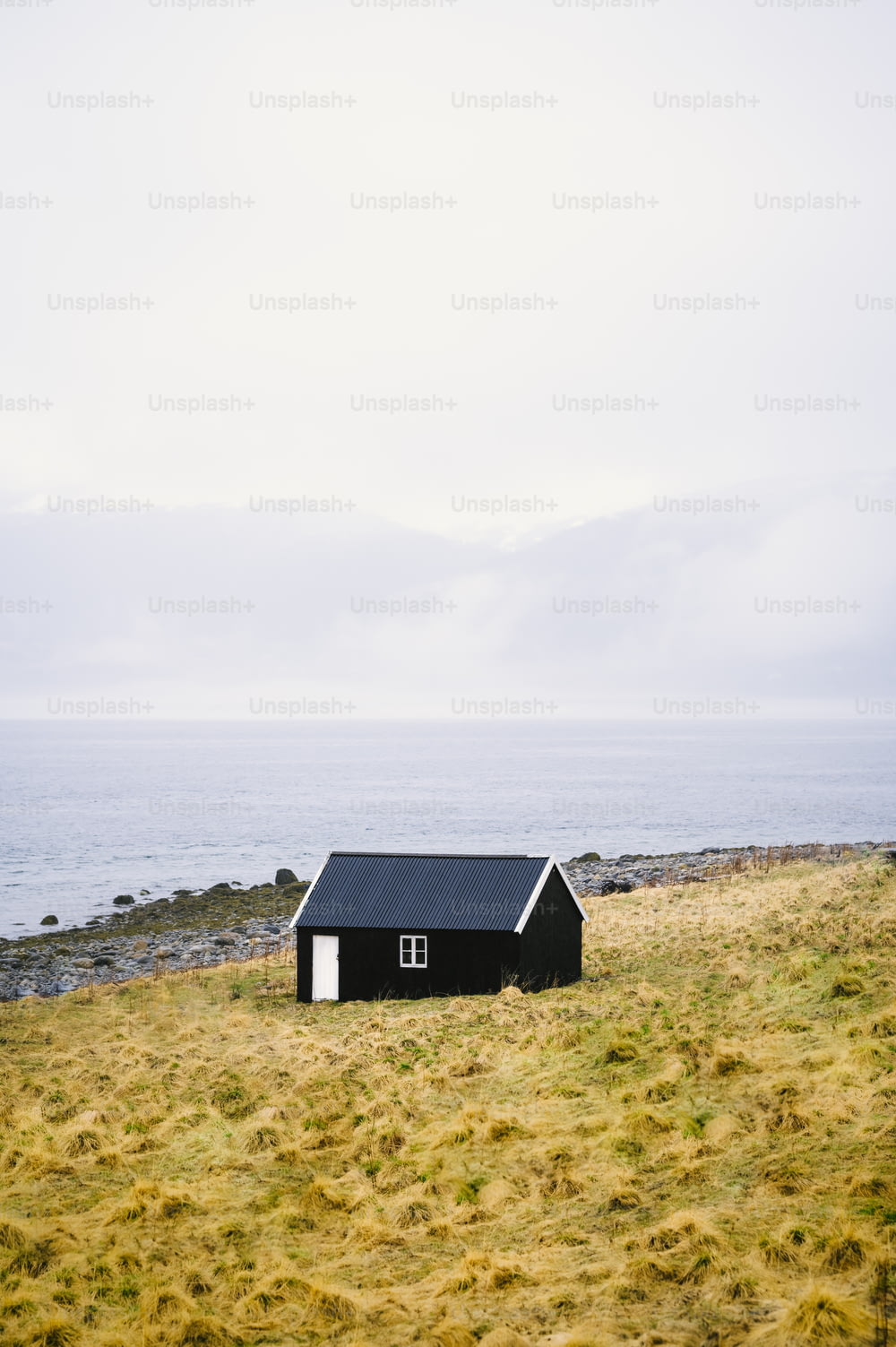 a small black house sitting on top of a grass covered field