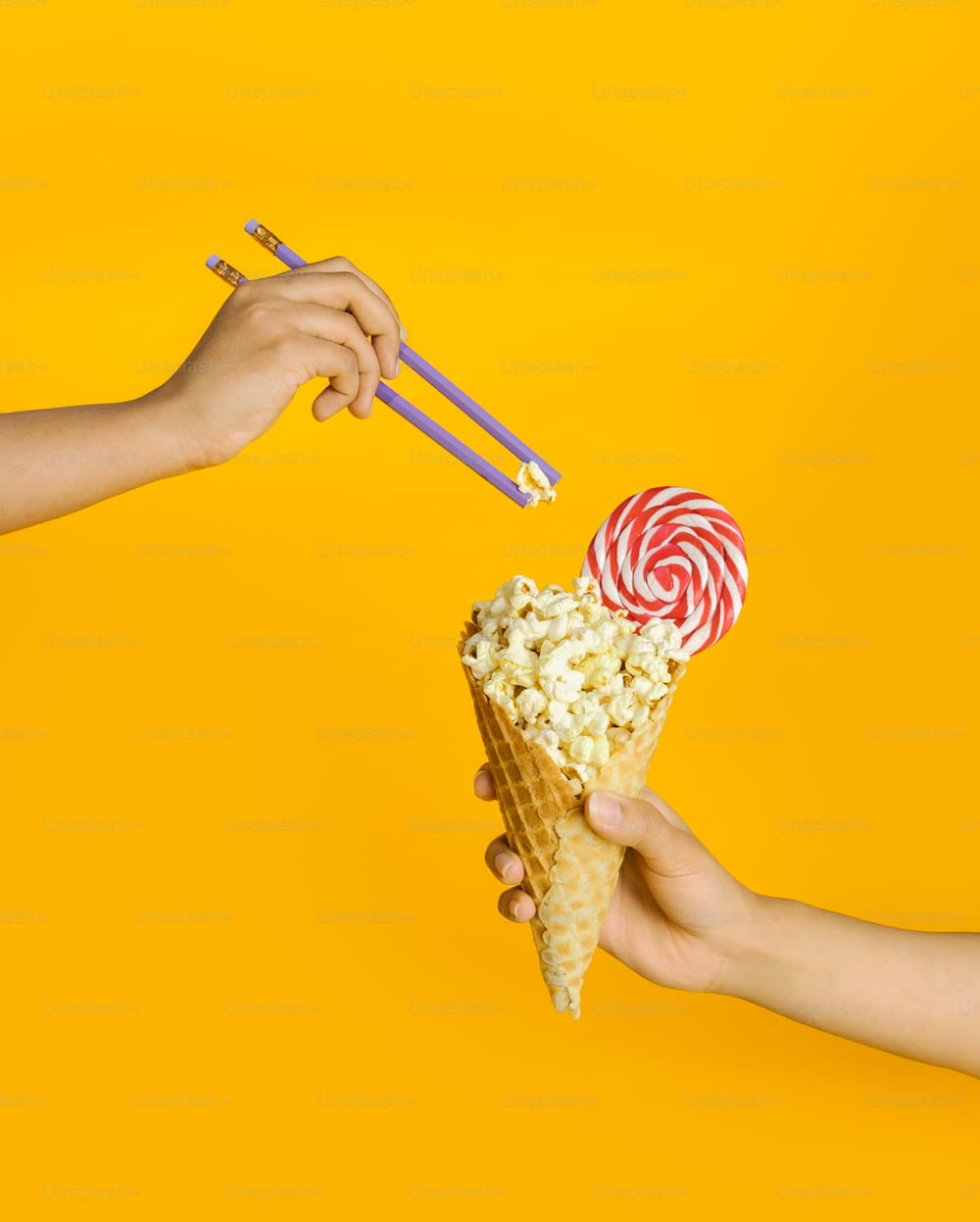 two hands holding a waffle cone filled with popcorn and two lollipops