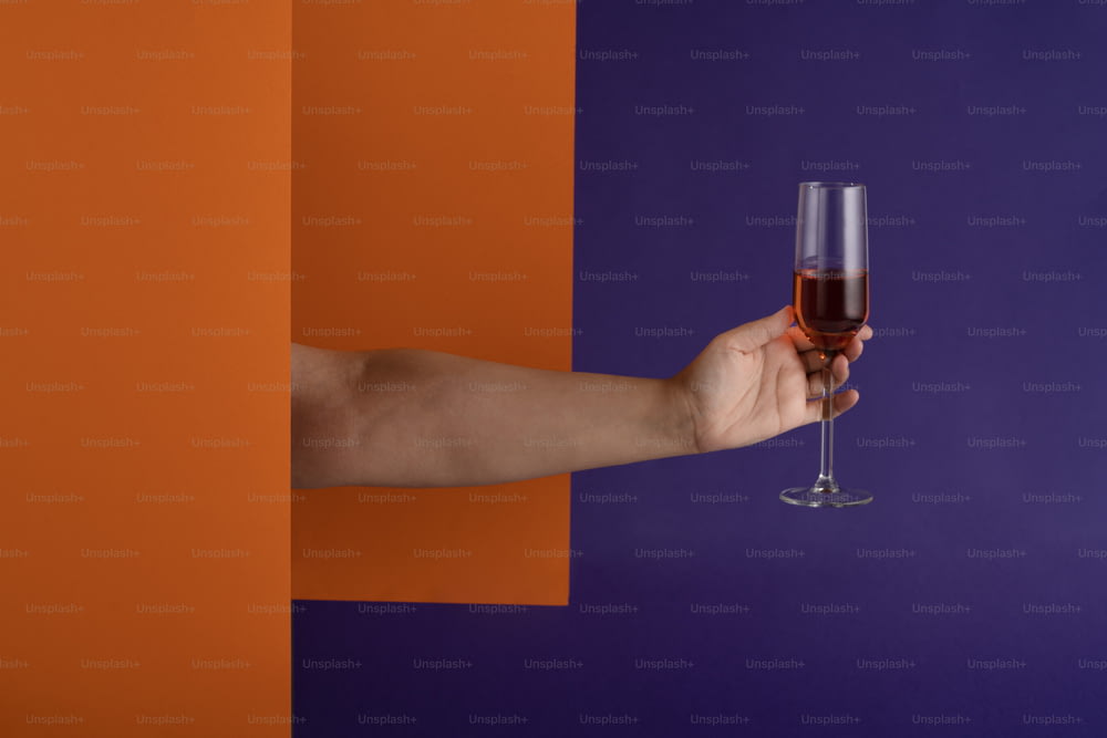 a hand holding a wine glass in front of a purple and orange wall