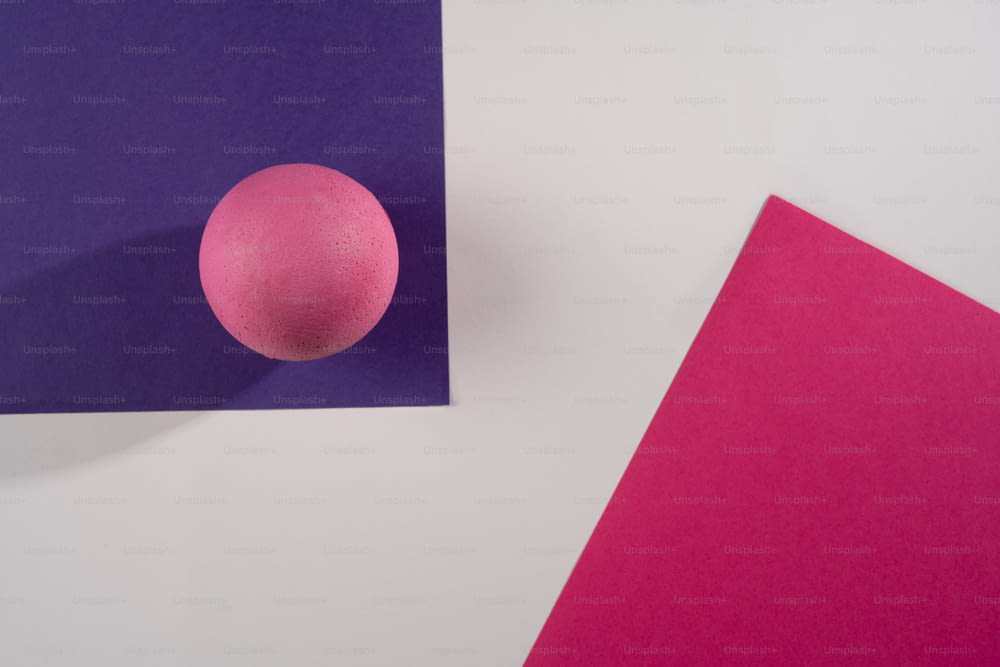 una palla rosa seduta sopra un pezzo di carta viola e rosa