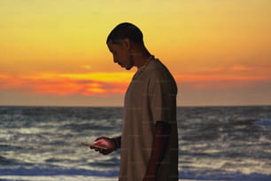 Un hombre parado en una playa sosteniendo un teléfono celular
