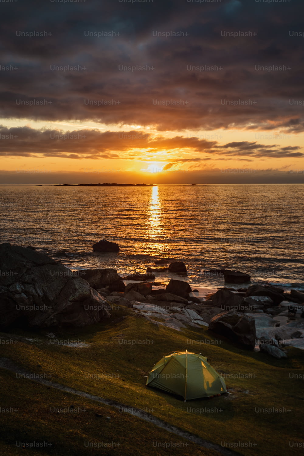 Uma tenda é montada em uma praia rochosa ao pôr do sol