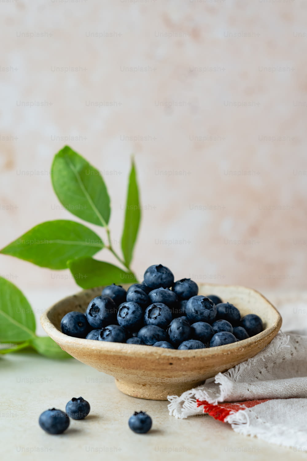a wooden bowl filled with blueberries next to a green leaf