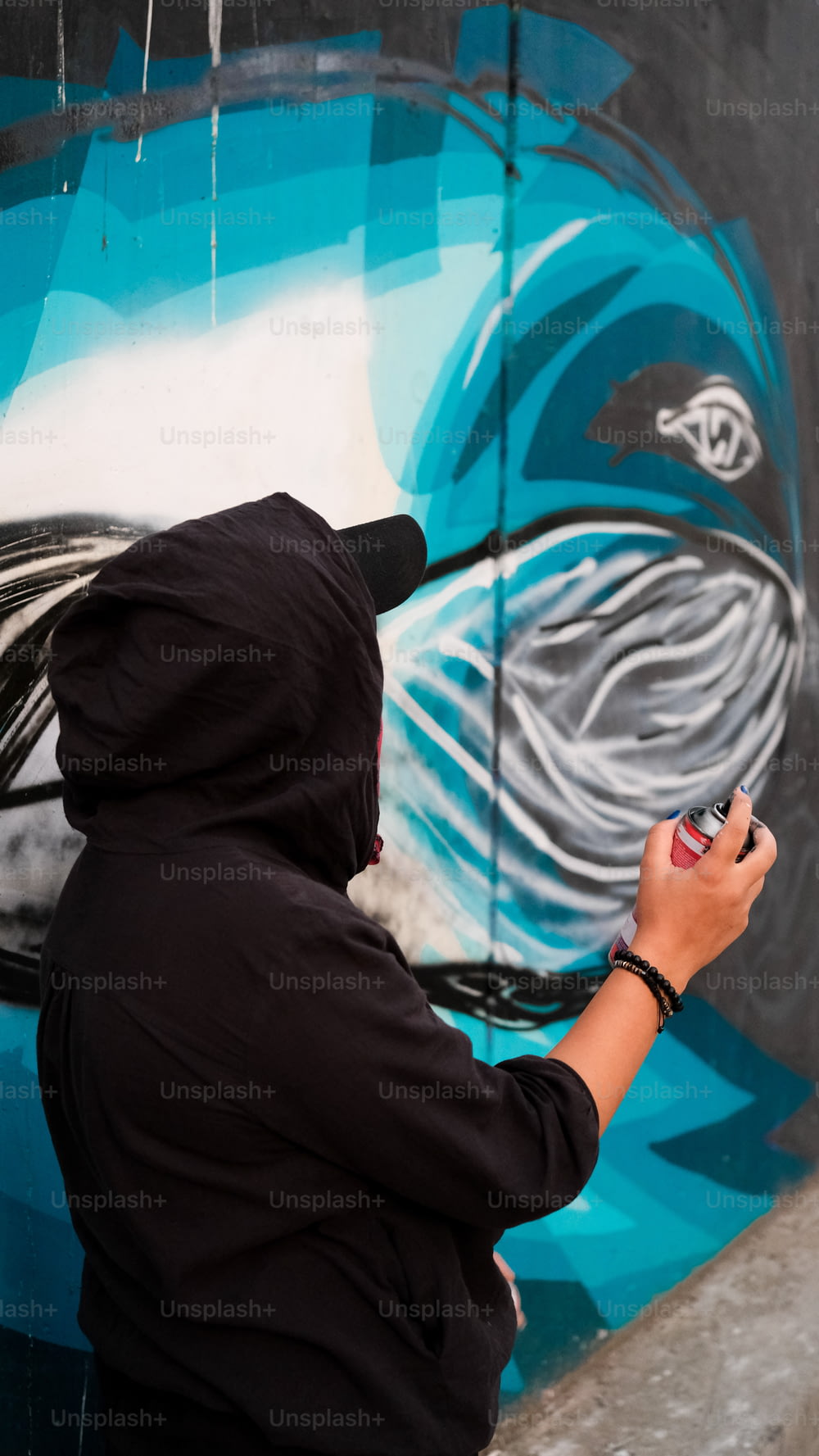 a person in a black hoodie is painting a mural