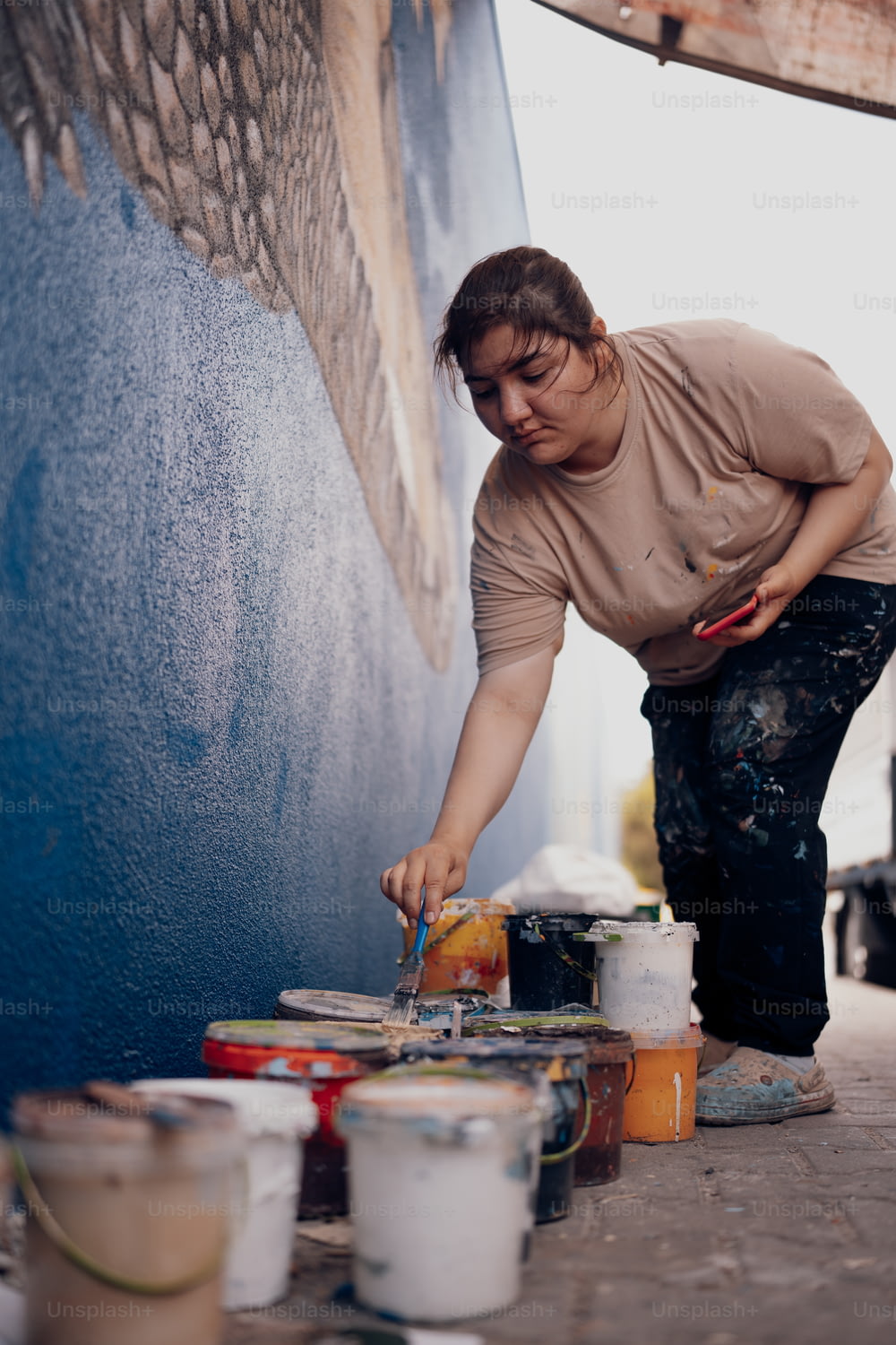 a woman is painting a wall with paint cans