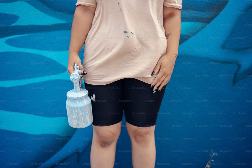 a woman standing in front of a blue wall holding a water bottle