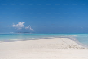 a sandy beach with clear blue water and a cloud in the sky