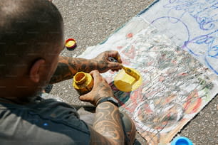 a man with tattoos is painting a picture on the ground