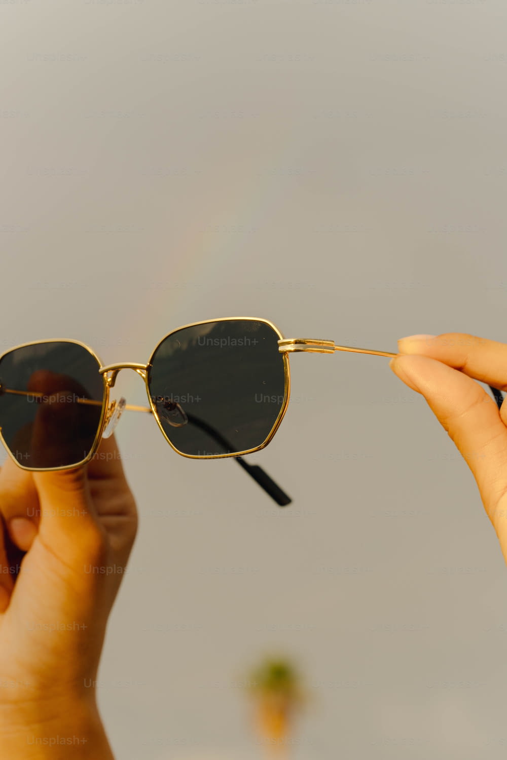 a person holding onto a pair of sunglasses with a rainbow in the background