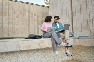 Un homme et une femme assis sur un rebord avec un ordinateur portable