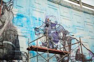 a man on a scaffold painting a mural on the side of a building