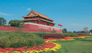 a large building with a red roof surrounded by yellow and red flowers