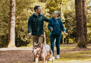 a man and woman walking a dog through a forest