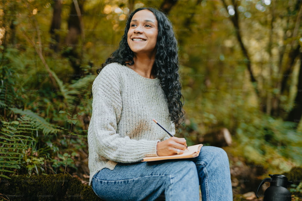 a woman sitting in the woods writing on a notebook