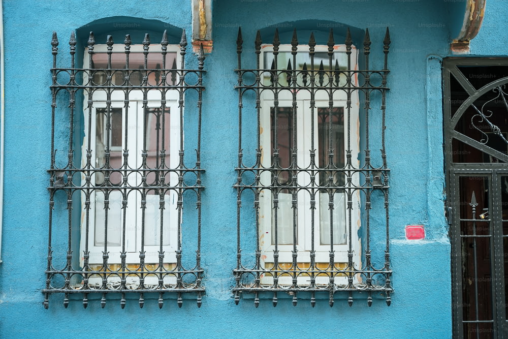 a blue building with two windows and iron bars