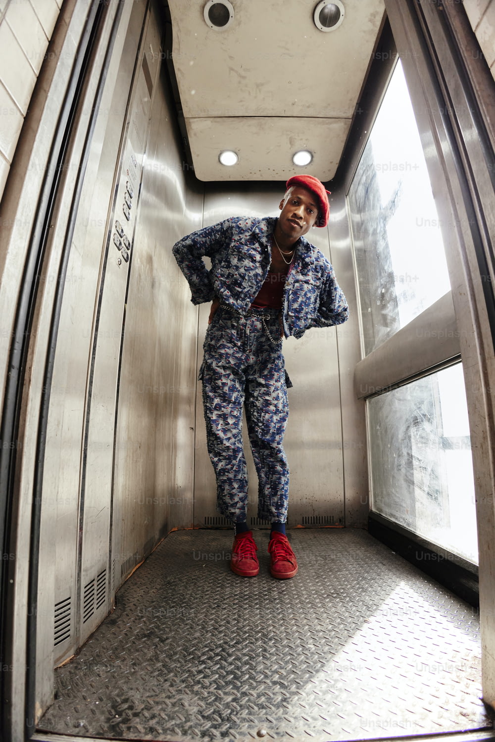a man in a red hat and blue jumpsuit standing in an elevator