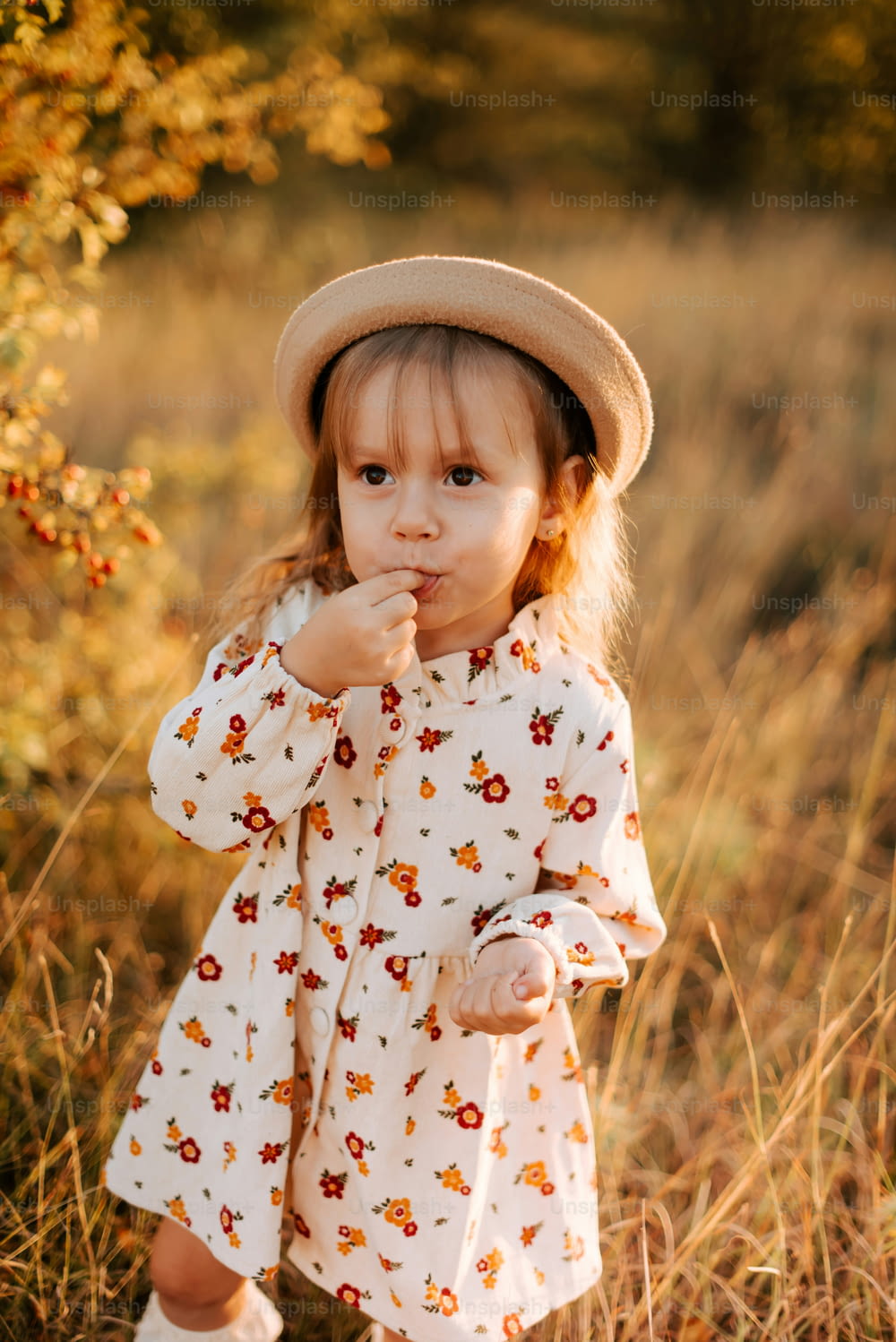 a little girl standing in a field with a hat on