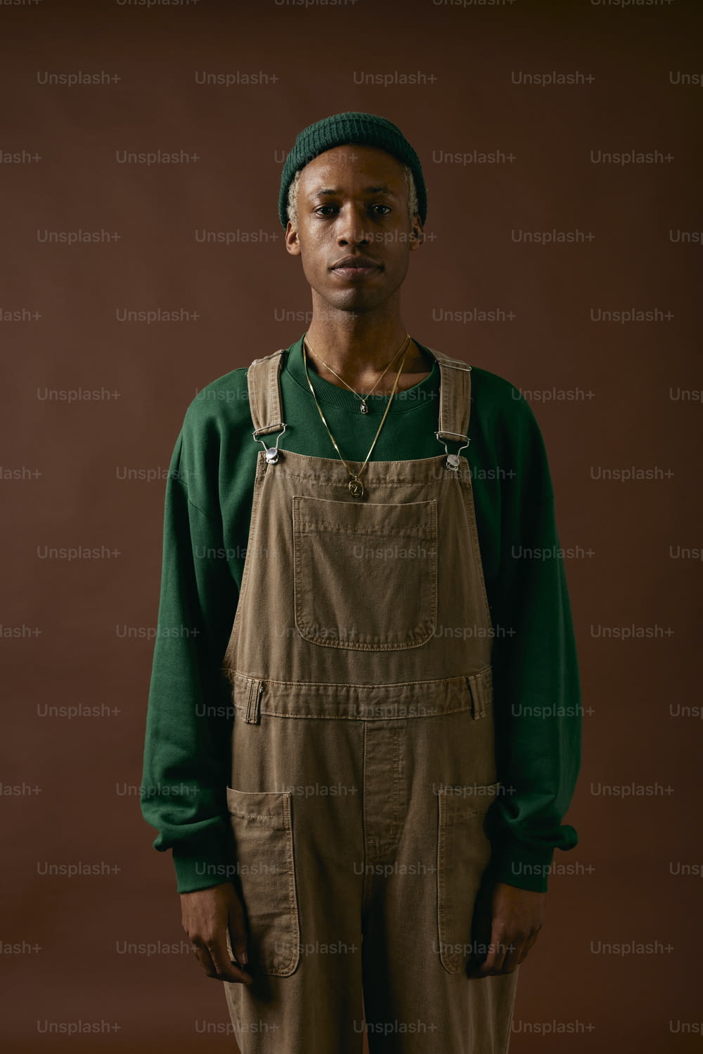 a man wearing overalls and a green sweater
