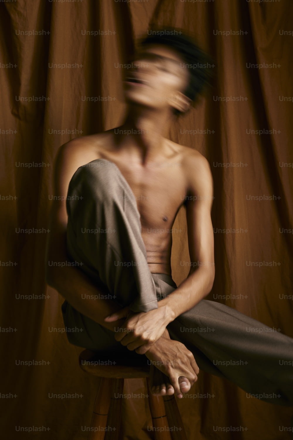 un homme torse nu assis sur un tabouret devant un rideau