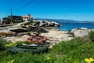 Small old lighthouse in the Illa de Arousa island in the Rias Baixas in Galicia, Spain, with some abandoned wooden boats in the foreground.