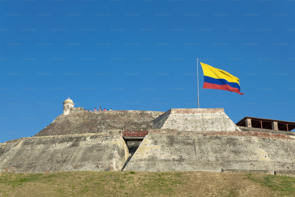 콜롬비아 국기가 콜롬비아 카르타헤나 데 인디아스에 있는 카스티요 산 펠리페 데 바라하스 요새의 풍화된 벽 위로 바람에 휘날리고 있습니다.