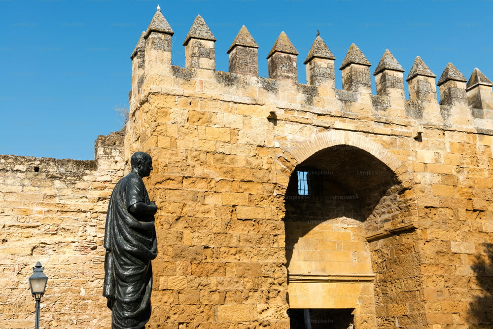 맑은 봄날 코르도바 구시가지를 둘러싸고 있는 중세 성벽에 있는 아랍어 문 중 하나(푸에르타 데 알모도바르)의 세부 사항, 그 앞에 철학자 세네카의 동상이 서 있습니다.